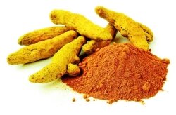 Tumeric roots sit on a pile of powered turmeric, both are an intense, warm yellow.