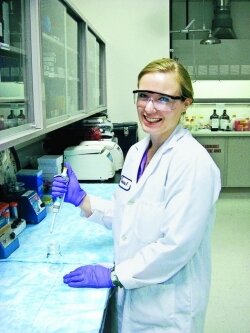 A woman in proper laboratory safety attire poses with a micropipette in a laboratory.